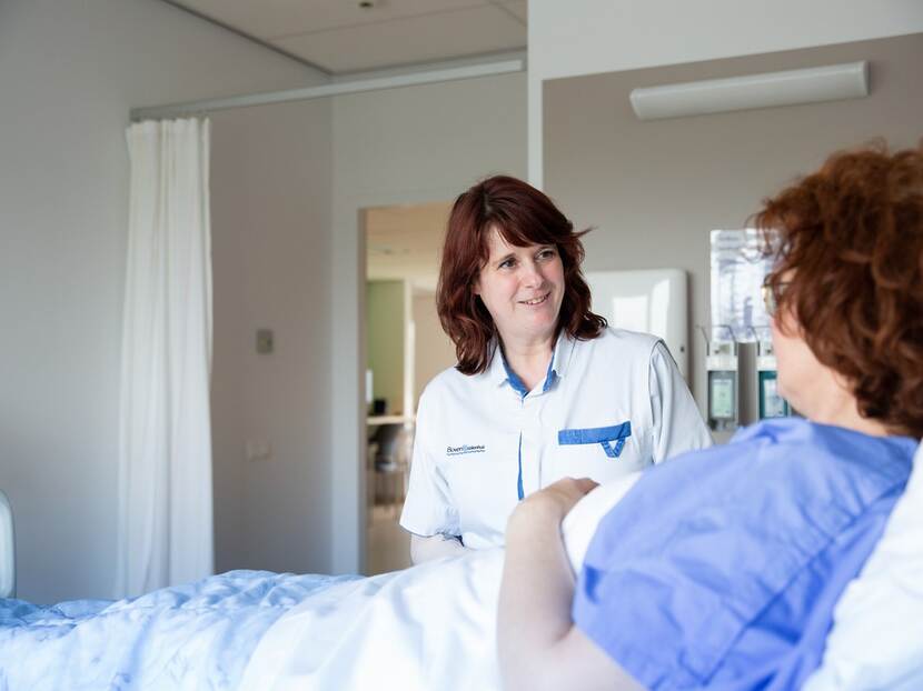 Verpleegkundige kijkt naar patient in bed.